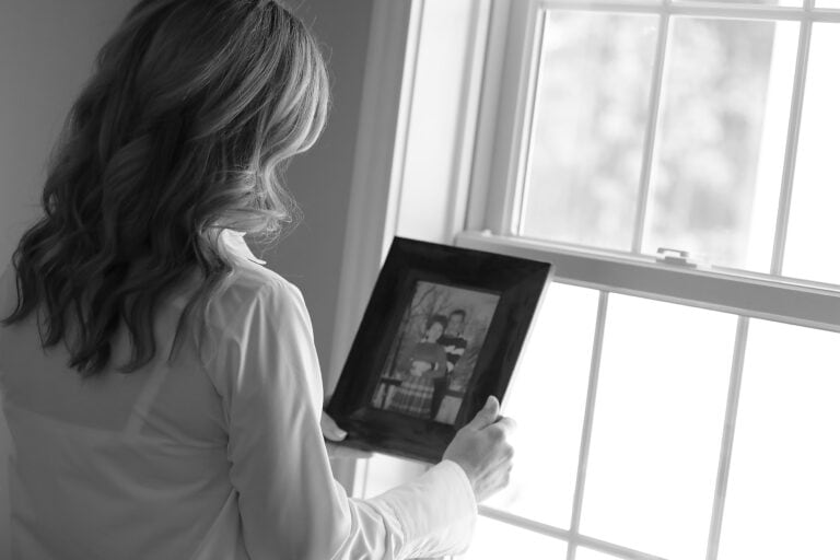 Black and white photo of a woman with long hair looking down at a photo of loved one who have passed.