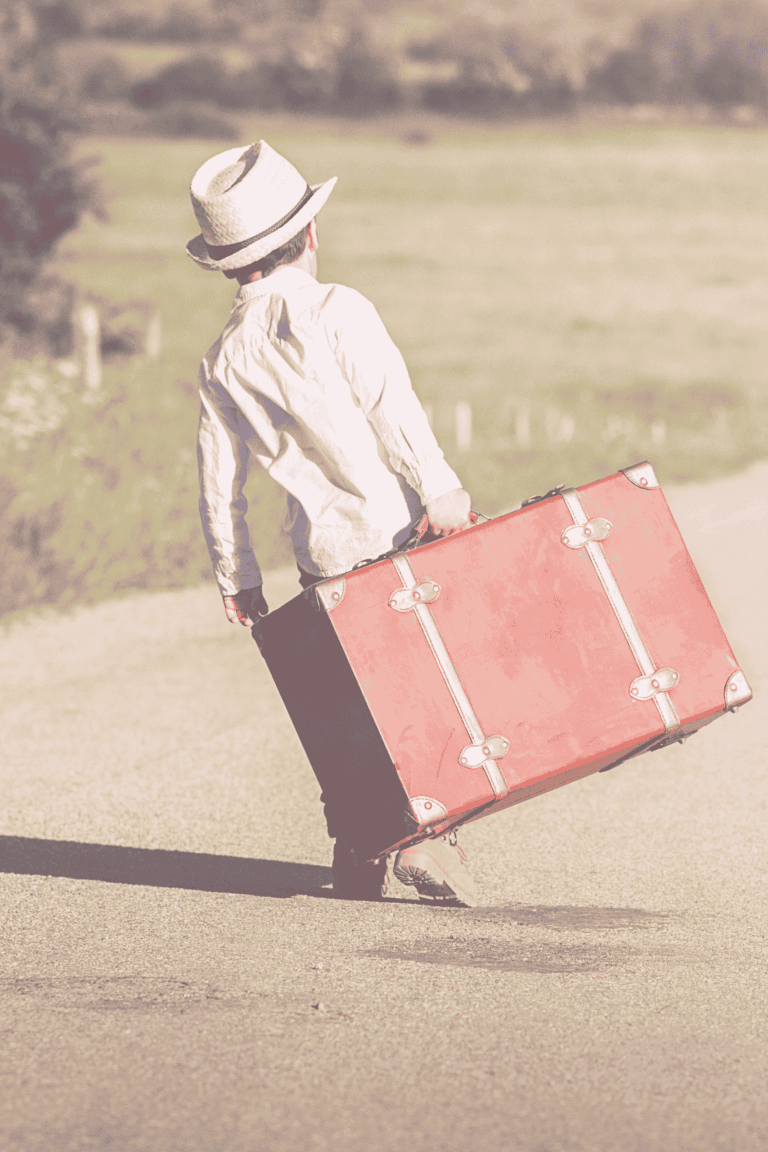 Little boy walking d, down a road with a big suitcase in his hand and hat on his head