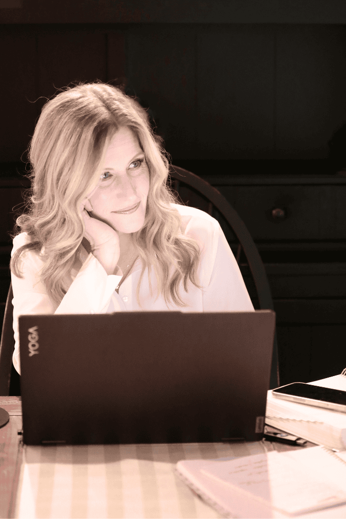 Woman sitting at laptop looking out resting her head on her hand