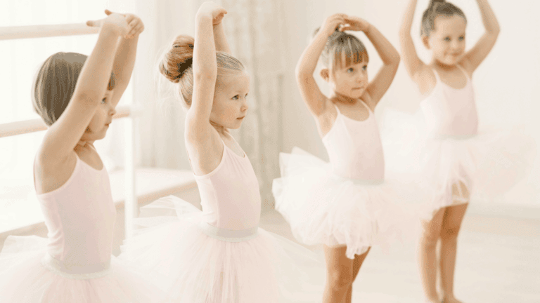 group of young ballerinas in pose during their dance class. They are wearing pale pink leotards and tutus.