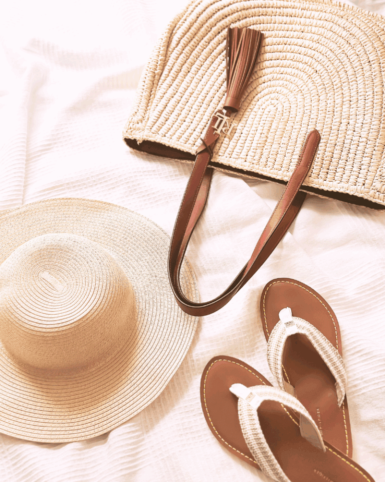 flatlay photo of a beach hat, flip flops and straw beach bag, all in neutral colors