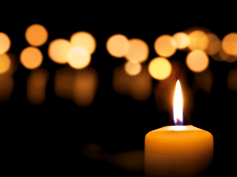A single lit candle with blurred bokeh lights in the background, symbolizing hope and remembrance.
