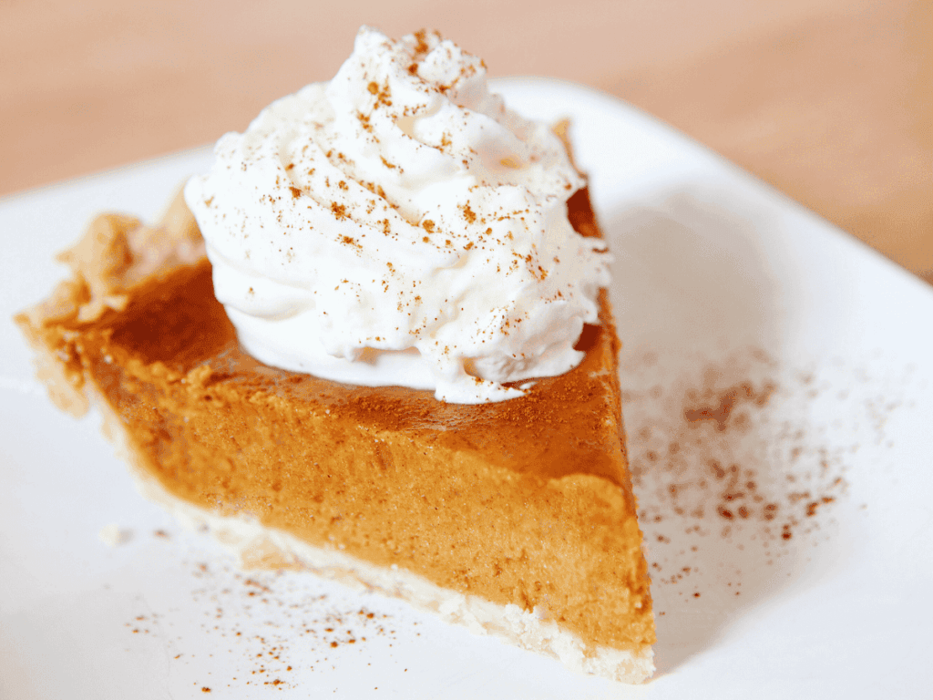Creamy pumpkin pie slice topped with whipped cream and cinnamon on a white plate.