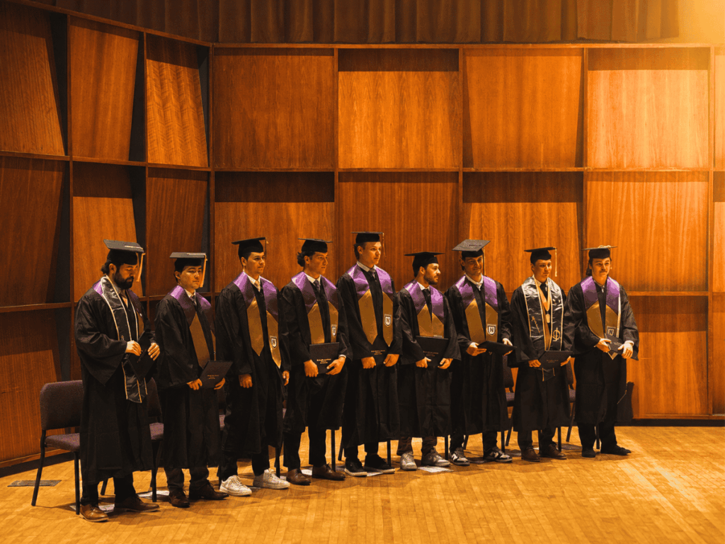Graduates in caps and gowns standing in a row during graduation ceremony.