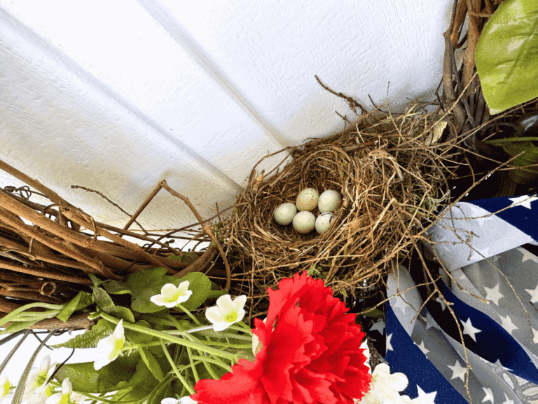 Decorative bird's nest with eggs, surrounded by green leaves and flowers.
