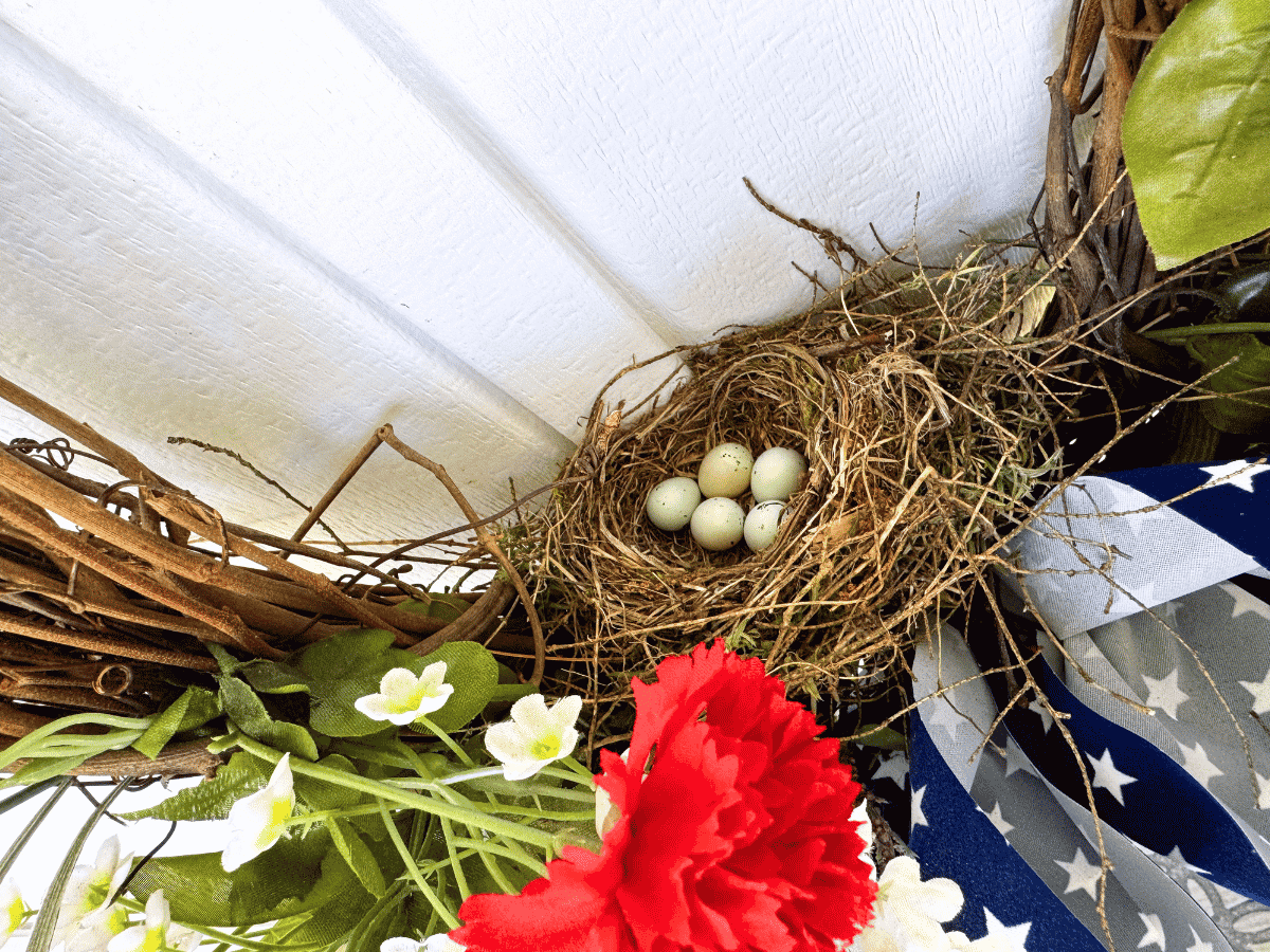 Decorative bird's nest with eggs, surrounded by green leaves and flowers.