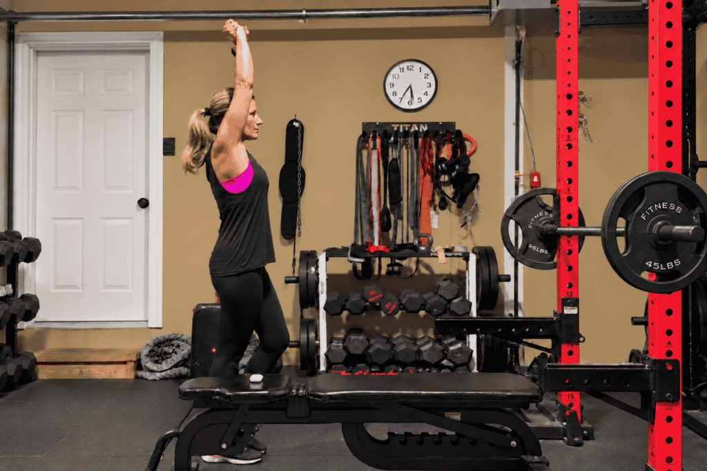 Woman stretching in home gym with weights and fitness equipment.