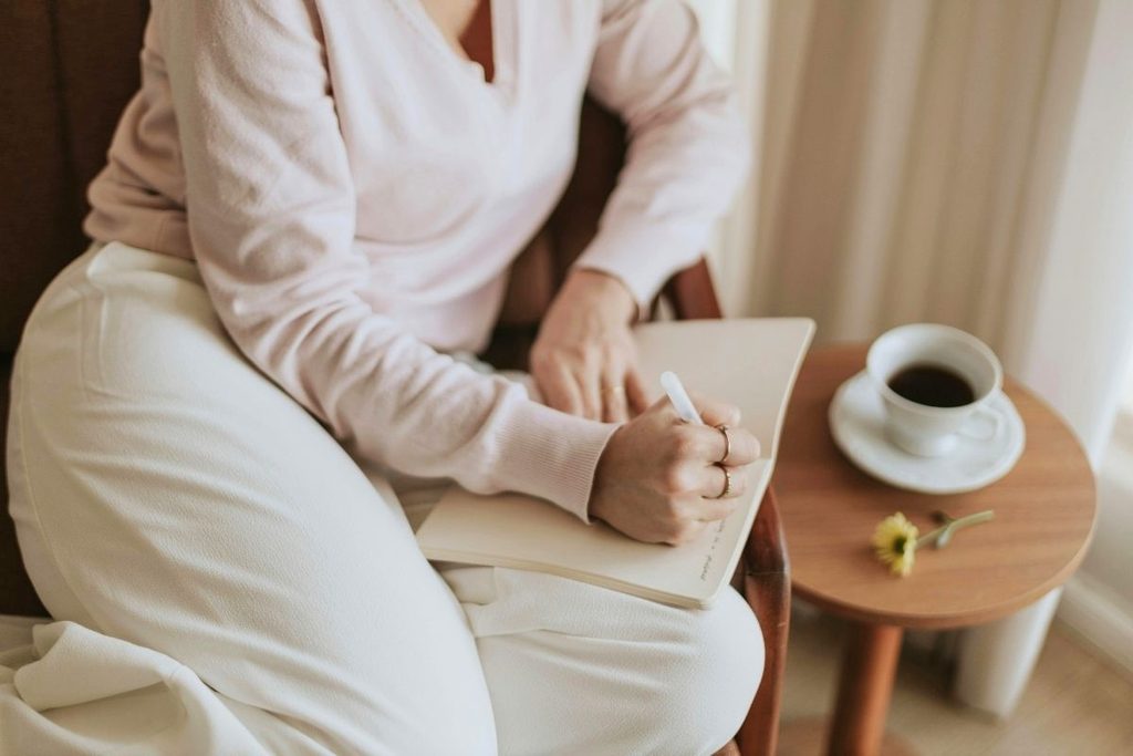 Woman writing in a notebook with coffee on a side table.